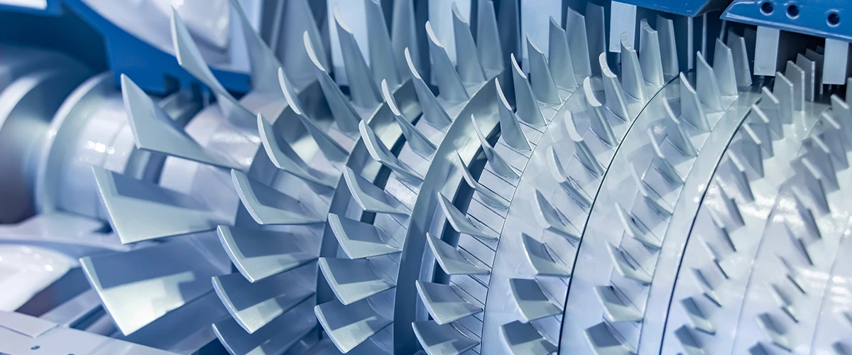 Nahaufnahme einer Turbine mit mehreren Reihen von Schaufeln, die präzise angeordnet sind. Die metallischen Strukturen reflektieren Licht und betonen die technische Komplexität der Bauteile.