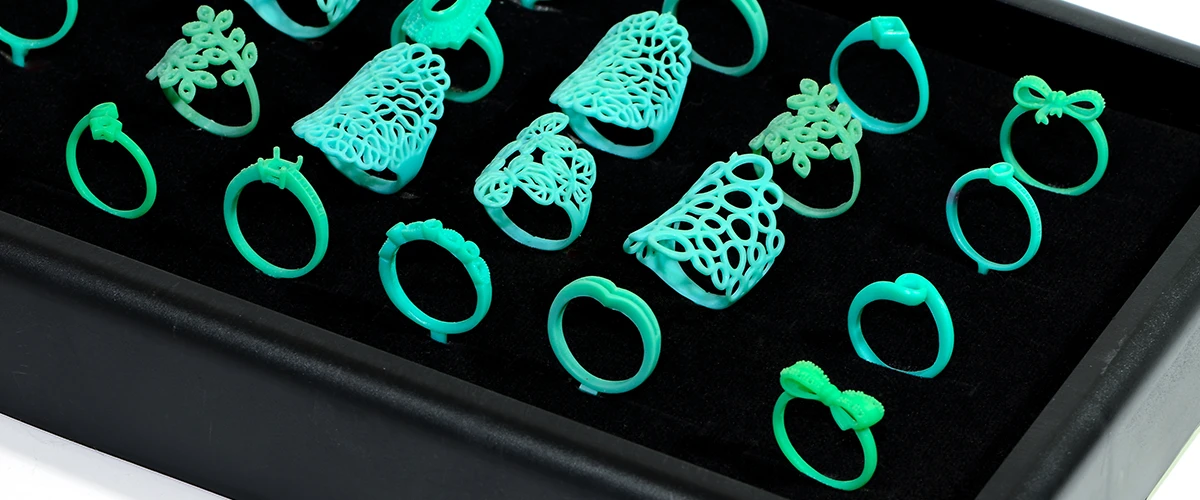 Several green wax models of rings with different, delicate designs are arranged in a black presentation box.