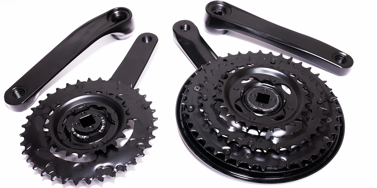 Two bicycle cranksets in black, each with multiple chainrings and the corresponding crank arms. The parts are shiny and detailed, ready for assembly.