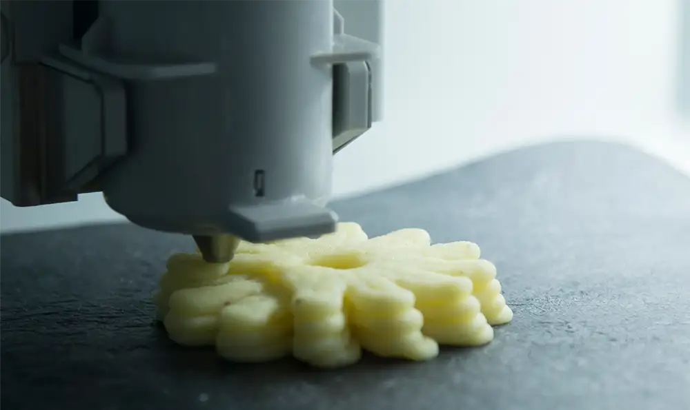 A 3D printer forms a flower-like structure out of dough