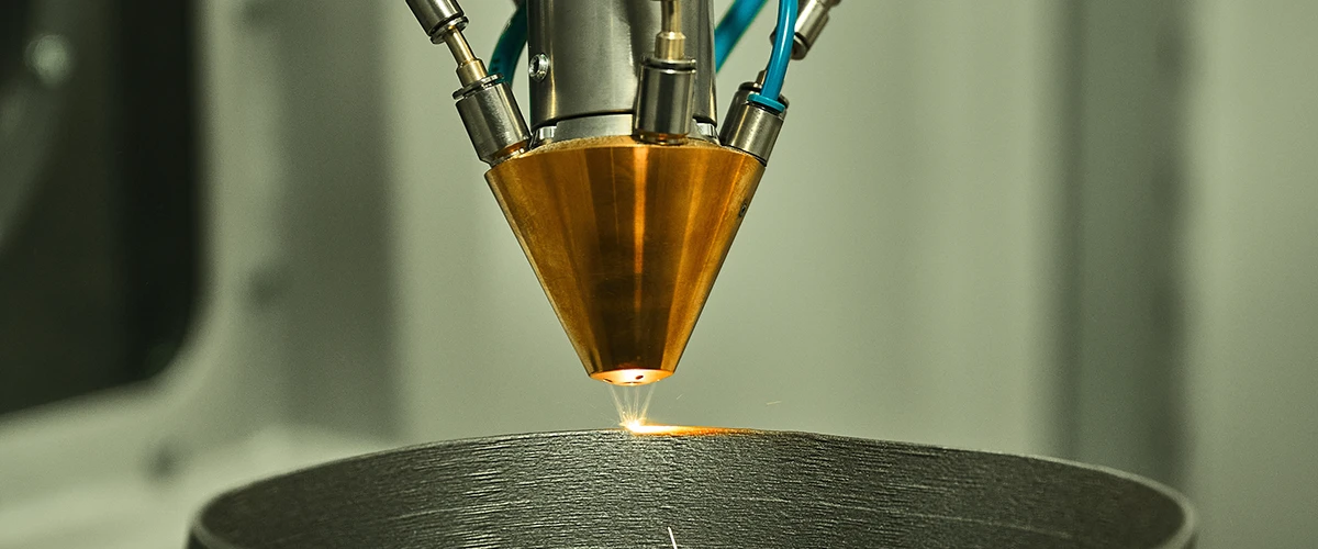 Close-up of a metal 3D print head applying precise layers to a workpiece. The gold print head operates with high accuracy and demonstrates modern additive manufacturing technology.