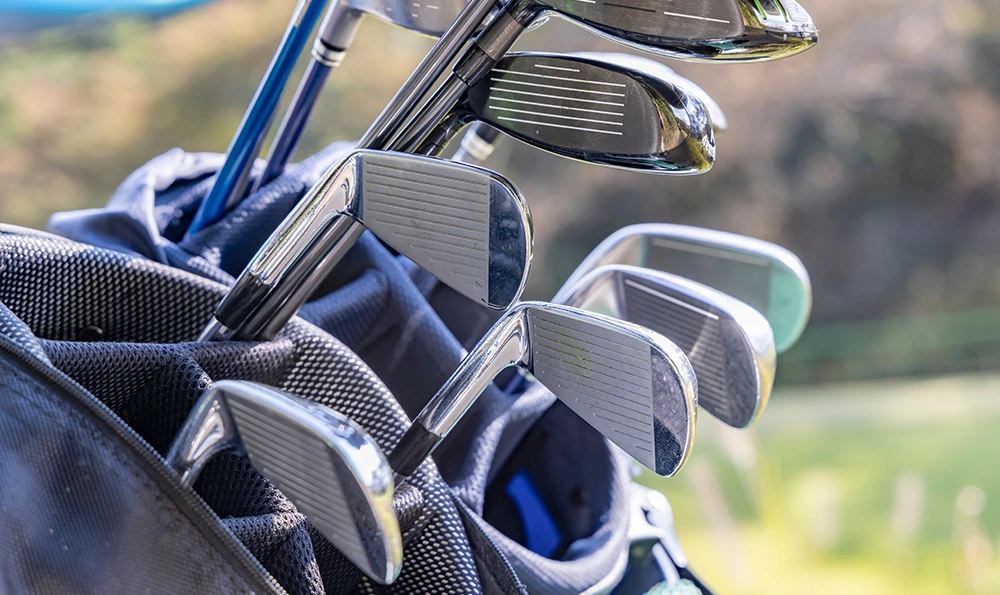 Several golf clubs with metal heads are in a golf bag on a golf course.