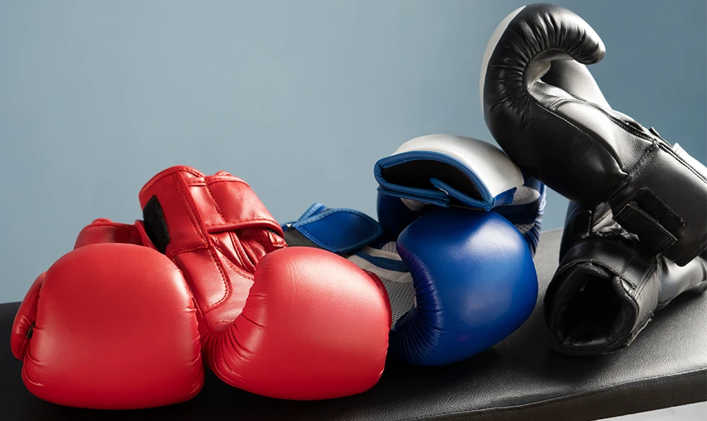 Three pairs of boxing gloves in the colors red, blue and black lie on a bench in front of a blue background.