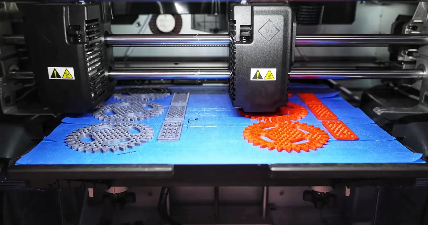 Various 3D printed gears and components made of orange and grey material on the print bed of a 3D printer.