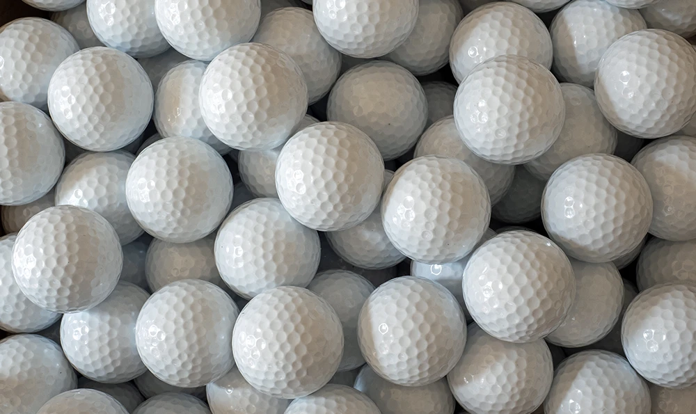 Many white golf balls with dimpled surfaces lie close together.