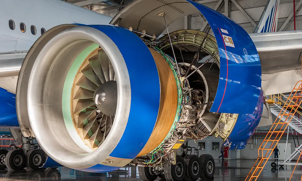 Close-up of an aircraft engine in a hangar, the cowling of which is open for maintenance. The complex internal mechanisms of the engine are visible.