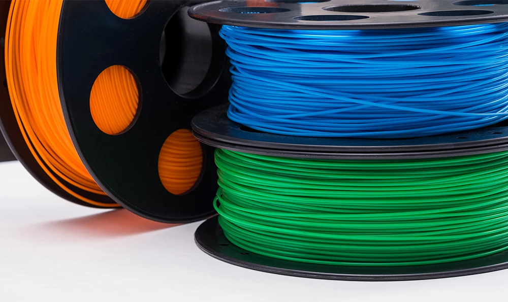 Three spools of 3D printing materials in different colors: orange, blue and green.