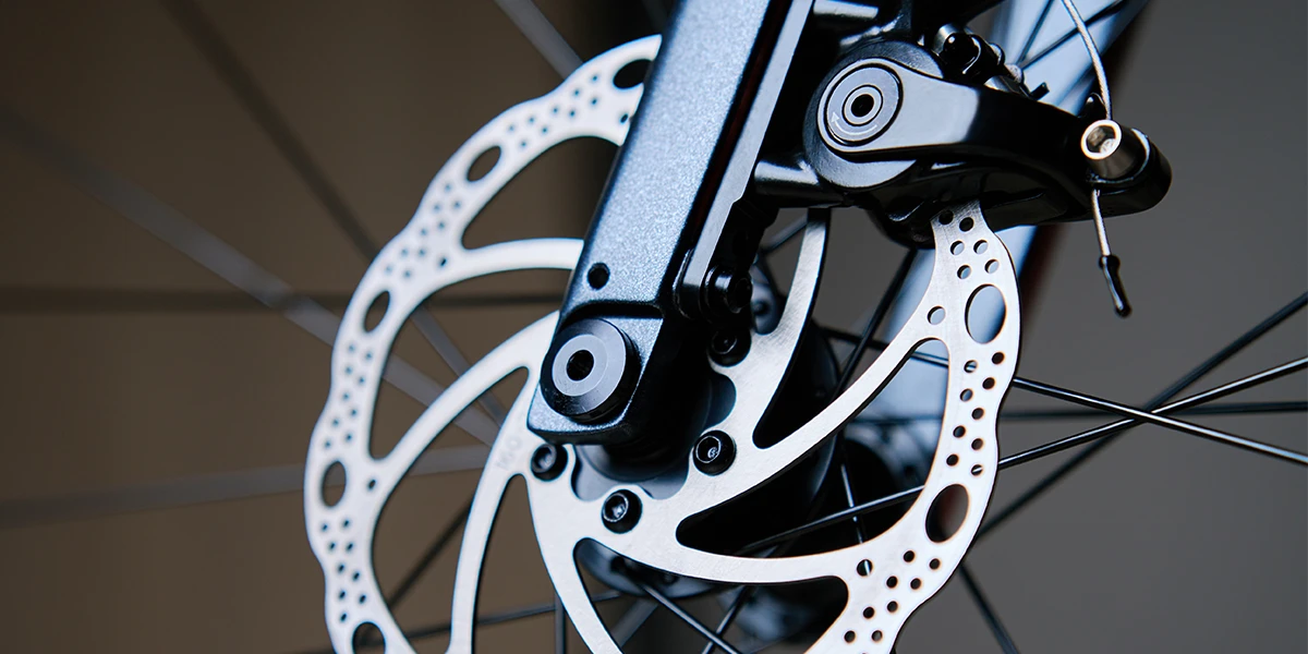 A detailed image of a bicycle brake with a metal brake disc and the brake caliper mounted on a bicycle frame.