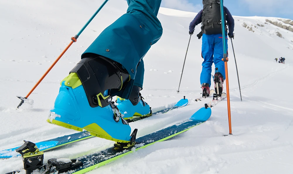 Two people climb up a snowy mountain with touring skis and ski poles.