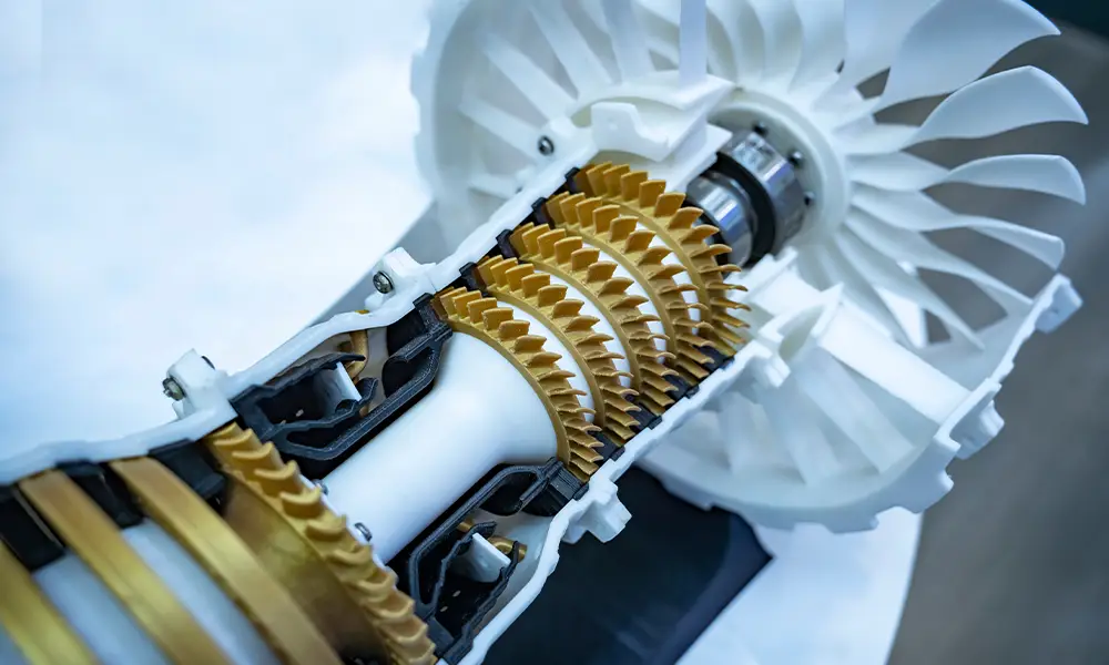 Cross-section model of an aircraft engine showing the internal components and turbine blades. The gold and white parts highlight the different functional areas of the engine.