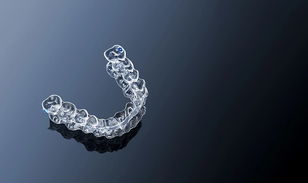 A clear brace or aligner rests on a dark, reflective surface.